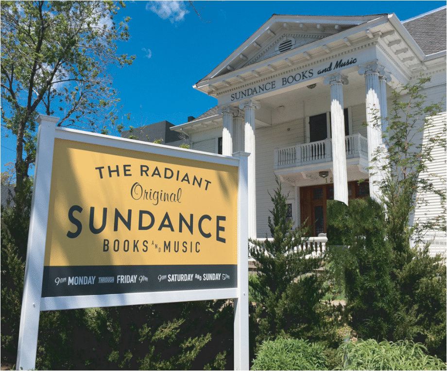 An outdoor photo of Sundance Books and Music is shown. The sign for the store is in the foreground of the image, with the actual store a bit farther behind at an angle.
